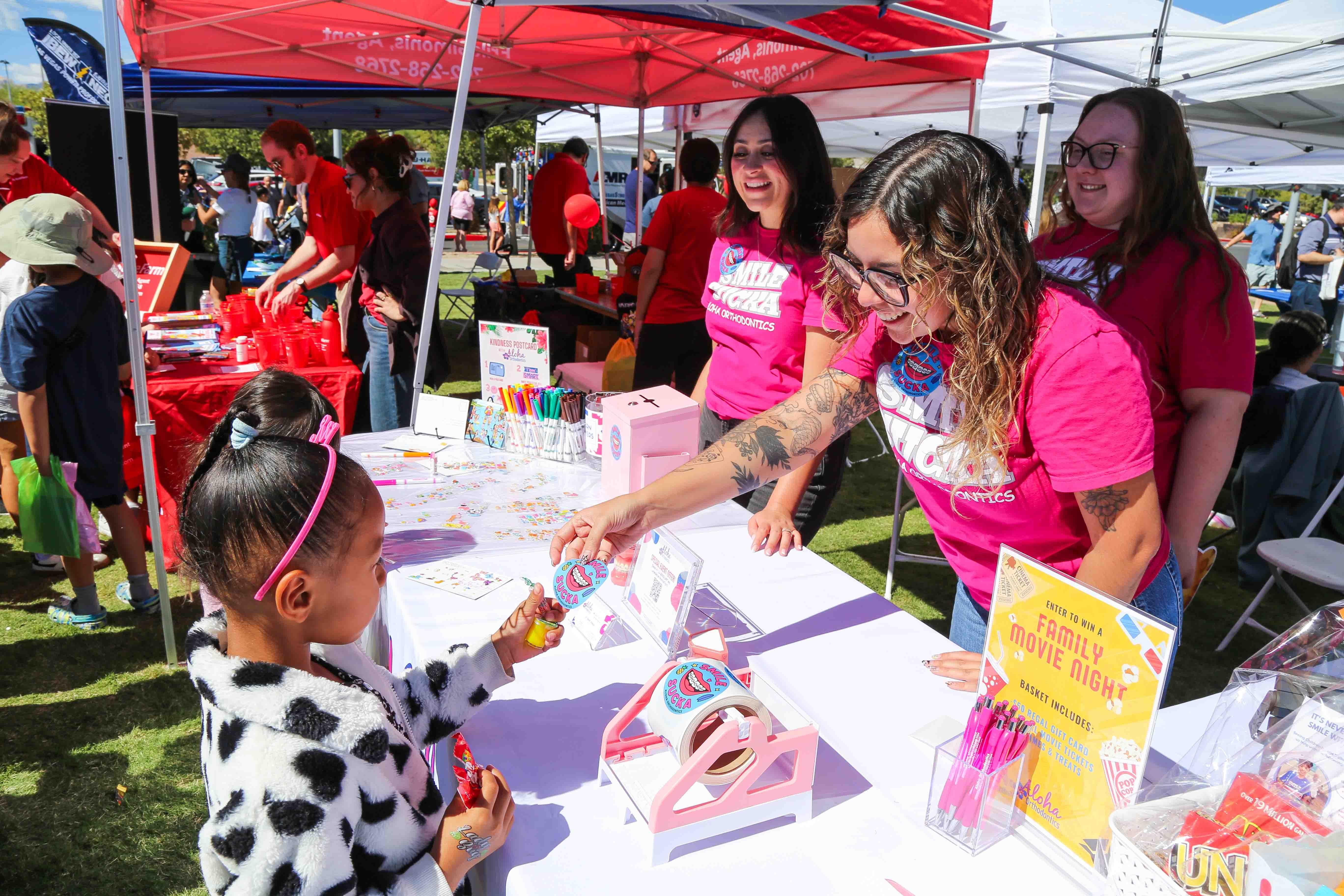 Ambassadors wearing pink T-shirts greet a child at an outdoor table