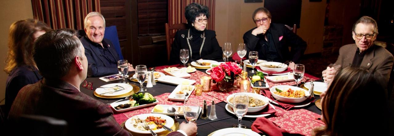 Camille Ruvo, Larry Ruvo, Lorraine Hunt-Bono, Dennis Bono, and Michael Severino sitting around a table at an Italian restaurant with various pasta dishes, water glasses, and empty wine glasses strewn about
