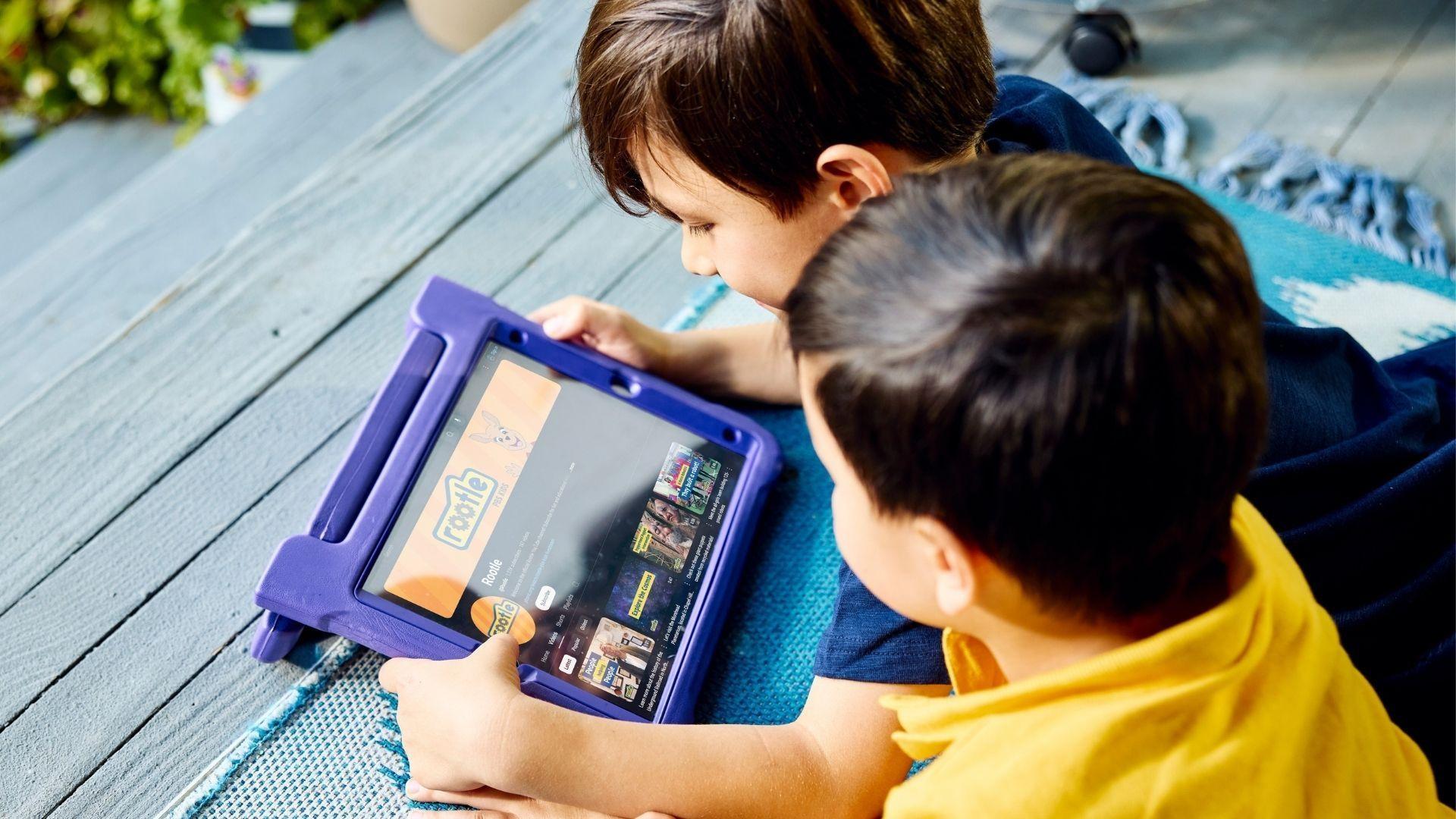 Two young children laying on their stomachs while visiting the Rootle YouTube channel on a tablet in a purple case.