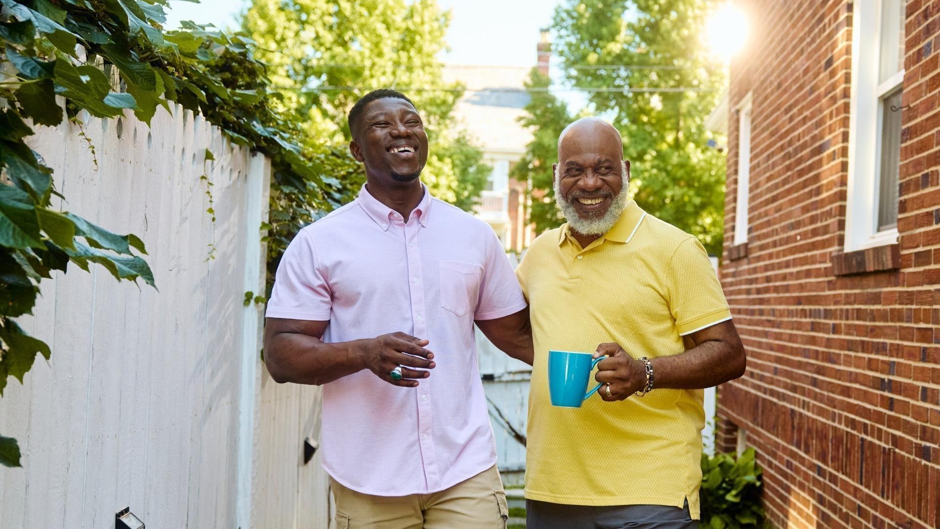 A father and a son laughing together while walking through a backyard.