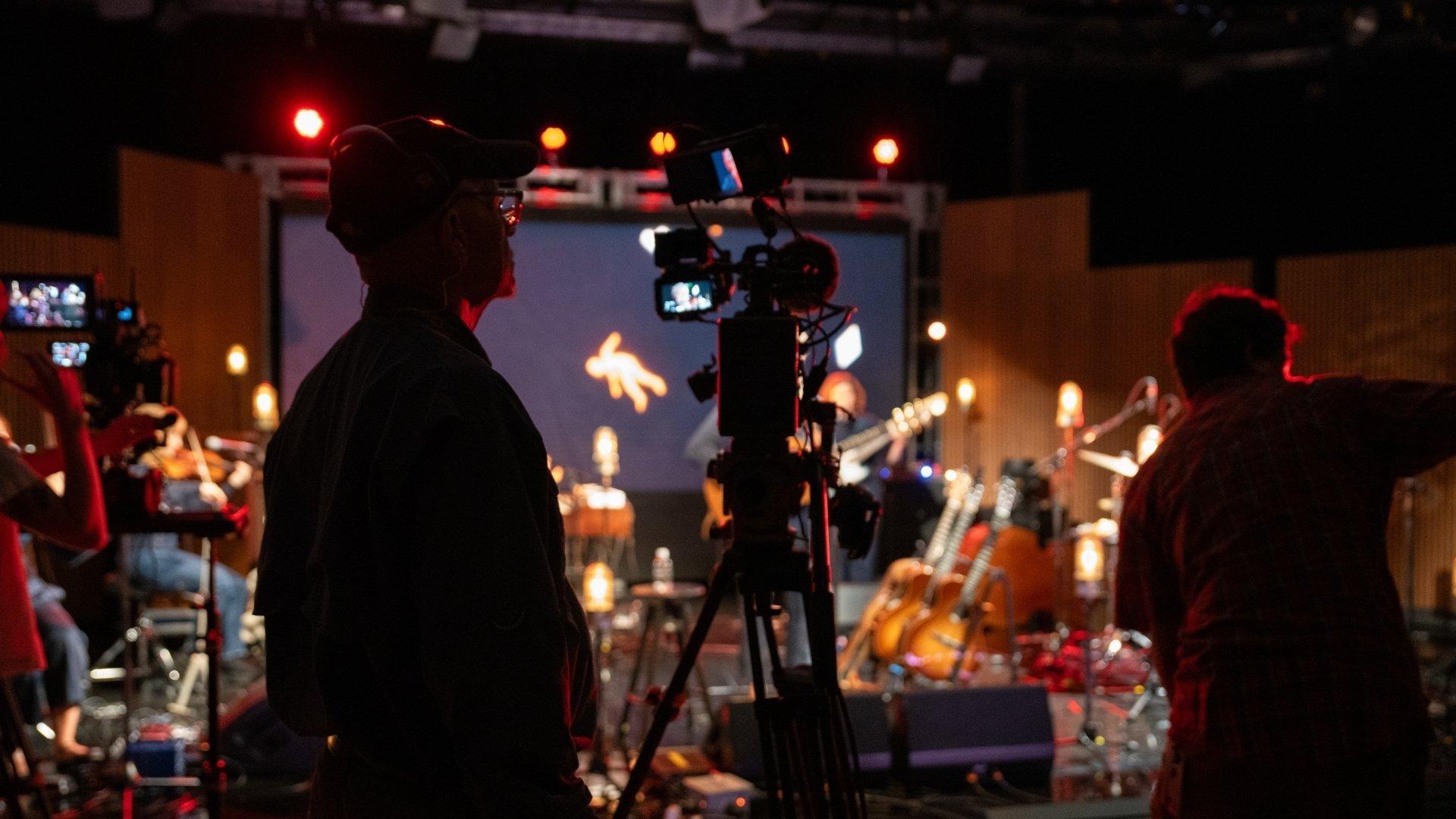 A look through a window to the PBS NC control room with the reflection of two people on the window's glass.